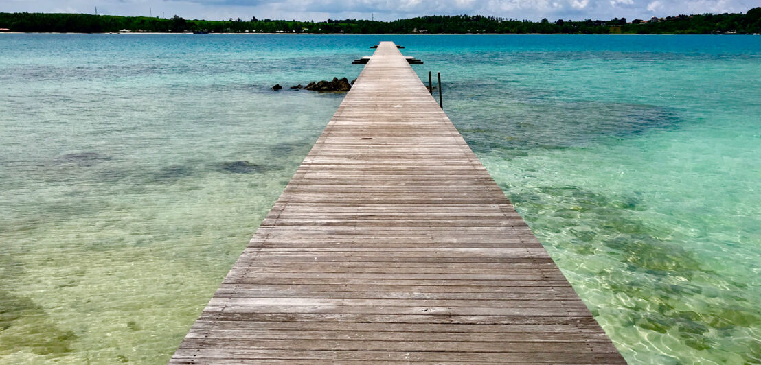 Langer Holzpier, der auf das Meer führt, mit Blick auf eine entfernte Insel