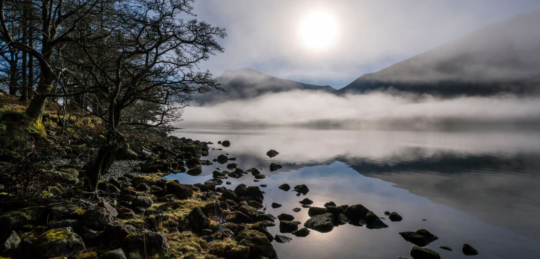 Nebelschwaden über einem See, im Hintergrund Berge 