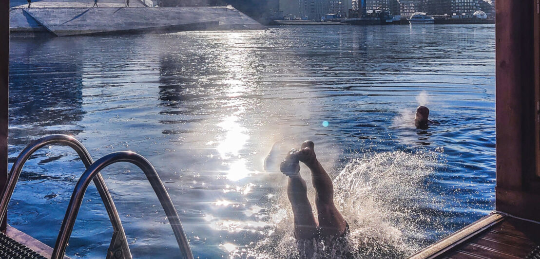 Zwei Personen baden vor einer schwimmenden Sauna im Hafen von Oslo