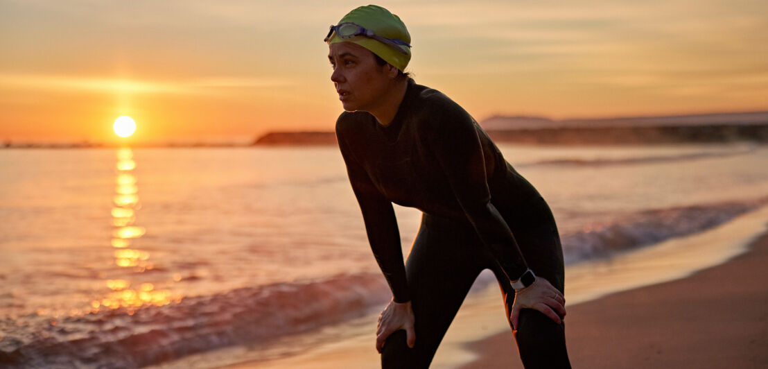 Eine Triathletin ruht nach dem Schwimmen in der Morgendämmerung am Strand aus