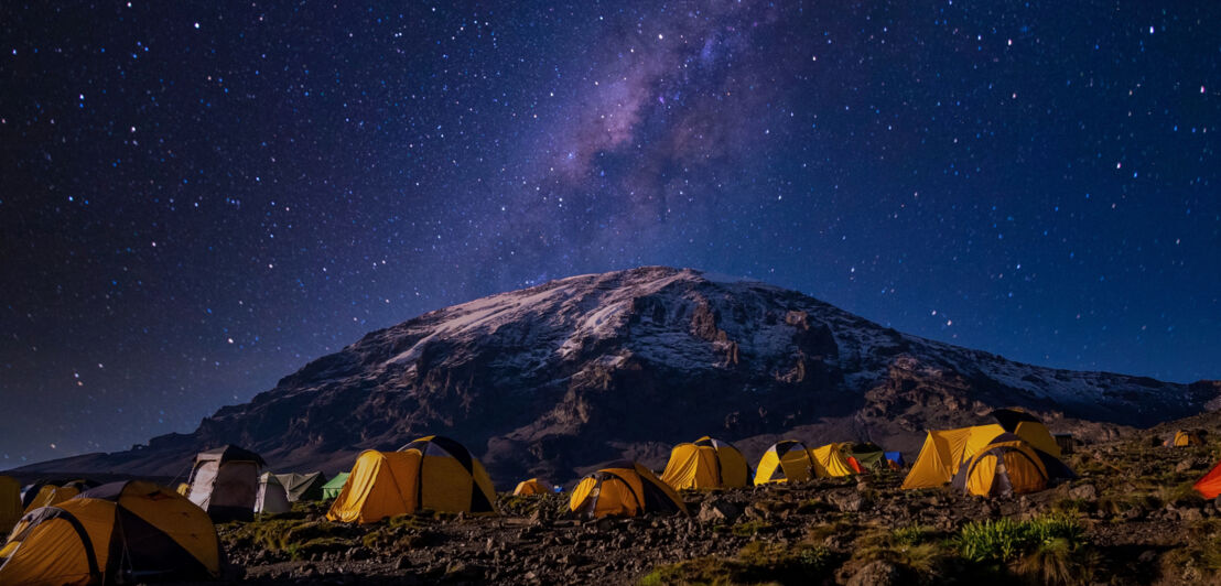 Gelbe Zelte auf einem Berggipfel unter Sternenhimmel bei Nacht