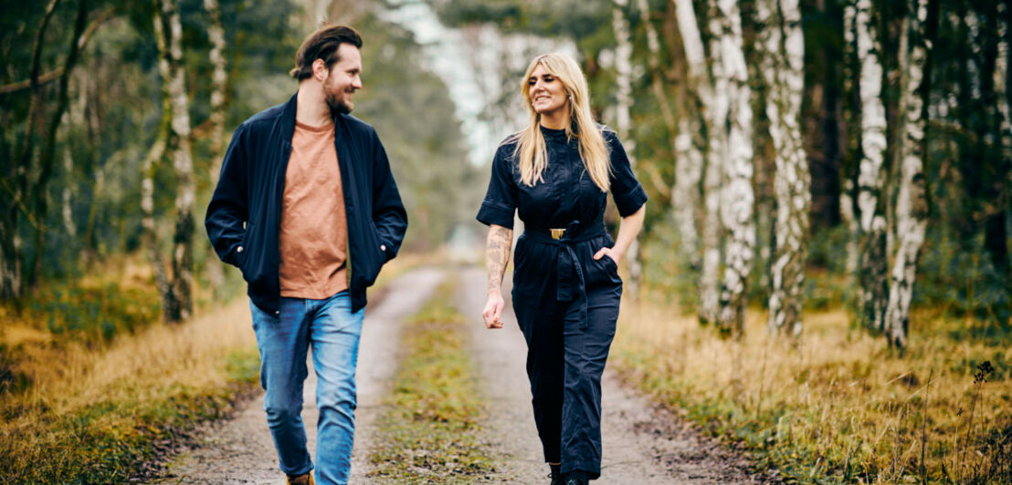 Tony Hohlfeld und Mona Schrader laufen über einen von Birken gesäumten Waldweg