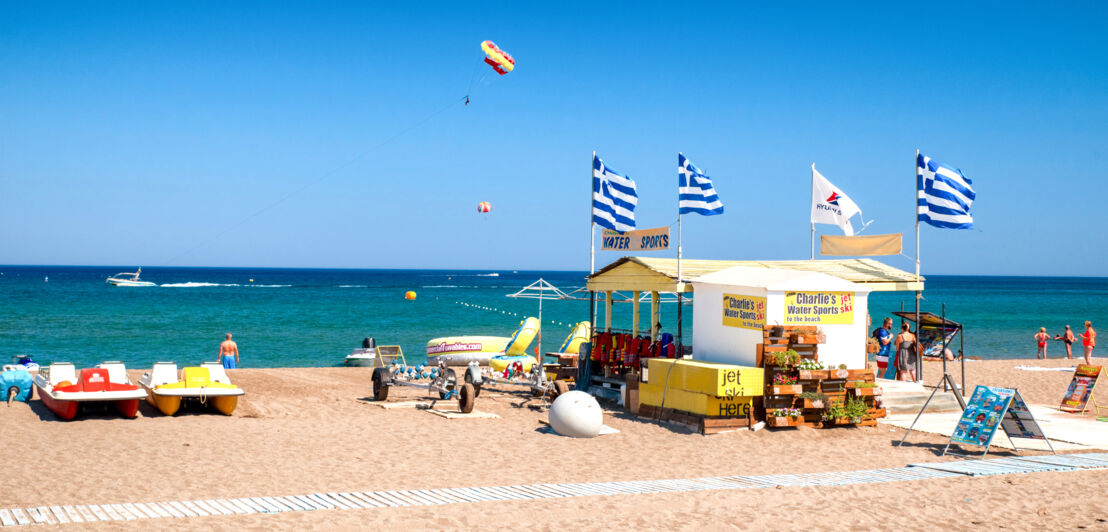 Strandhütte mit blauweißen Fahnen an einem Strand mit trükisfarbenem Meer