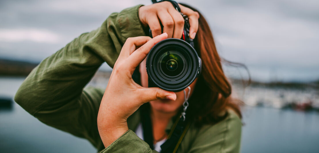 Nahaufnahme einer Person, die durch ihre Kamera auf den Fotografierenden blickt