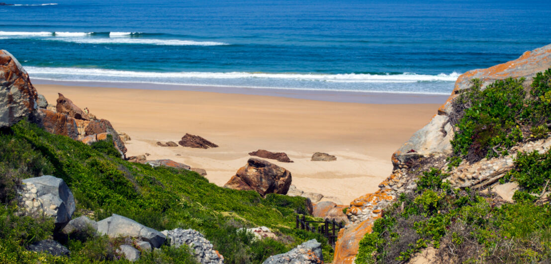 Blick von einem Felsen auf einen Sandstrand in einer menschenleeren Bucht, umgeben von wider Natur