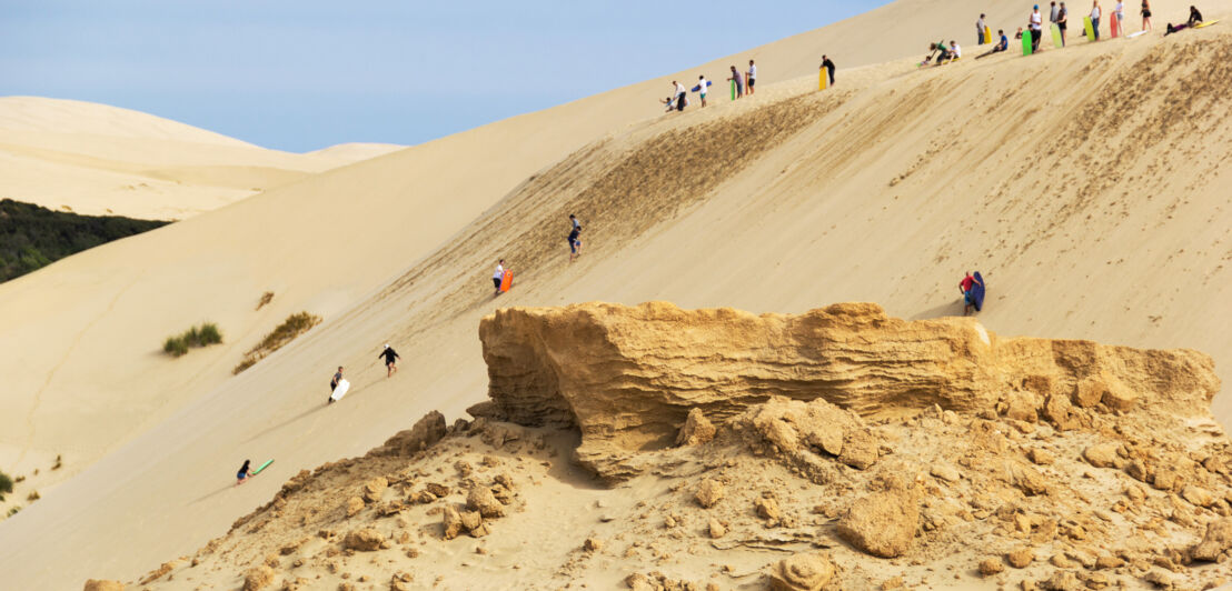 Mehrere Personen auf Sandboards am Abhang einer Sanddüne