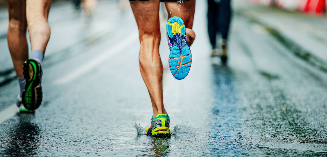 Aufnahme von drei trainierten Beinpaaren, die auf einer nassen Straße joggen