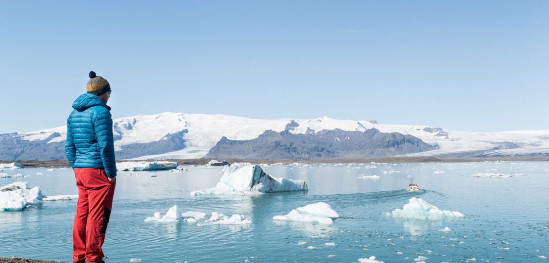 Eine Person blickt auf die Eisberge in der Gletscherlagune Jökulsárlón in Island.