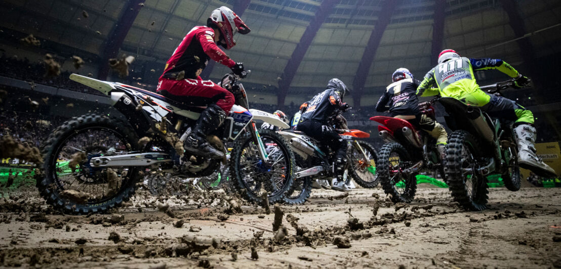 Mehrere Personen fahren mit ihrem Motocross in einer Halle neben- und hintereinander