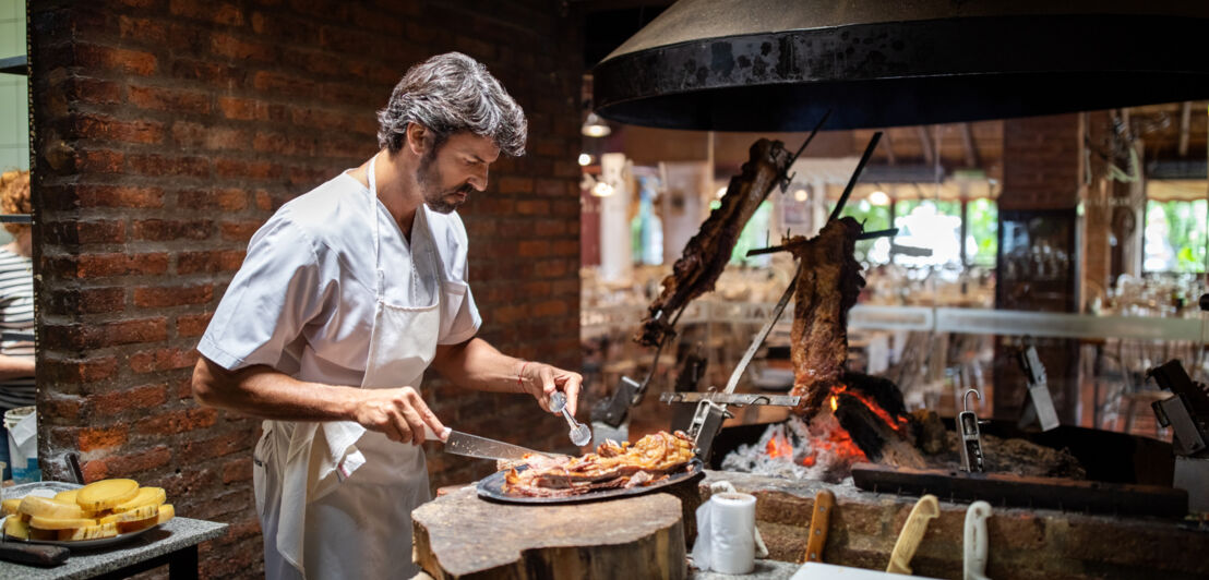 Ein professioneller Koch bereit Fleisch neben einem offenen Grill in einer Restaurantküche zu