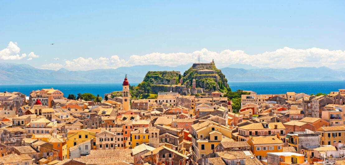 Blick über mediterrane Häuser sowie einen Hügel, auf dem eine kleine Burg zu sehen ist