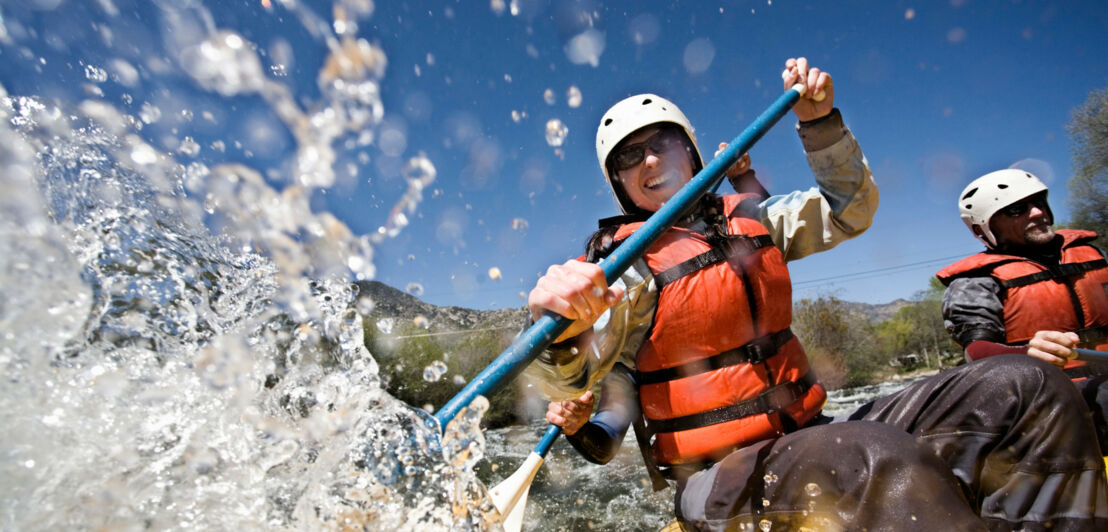 Zwei Personen in Schwimmweste und mit Helm beim Rafting