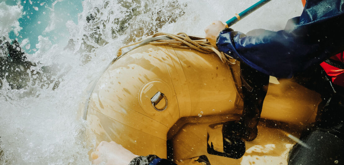 Detailaufnahme von einem Schlauchboot, in dem zwei Personen sitzen und ihre Paddel ins Wasser stoßen