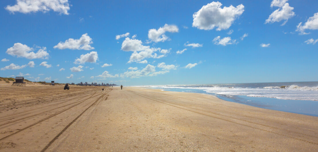 Panoramaaufnahme eines weitläufigen Sandstrandes unter blauem Himmel mit vereinzelten Kumuluswolken