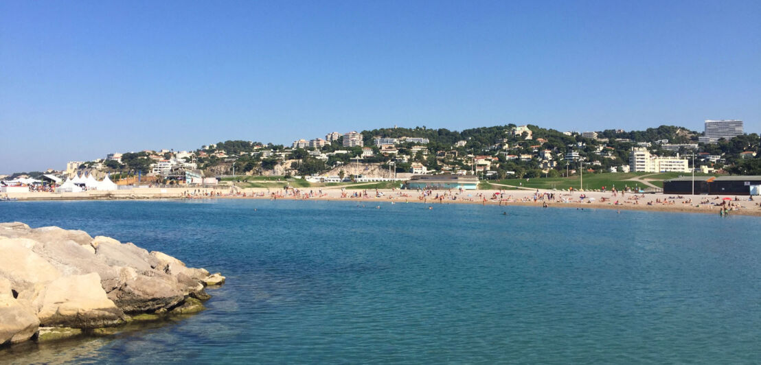 Meer im Vordergrund, weiter hinten Strand und eine hügelige Landschaft mit Häusern