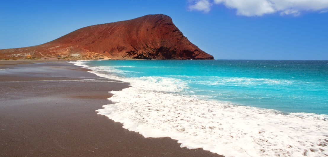 Weitläufiger Strand mit dunklem Sand und einem roten Felsen