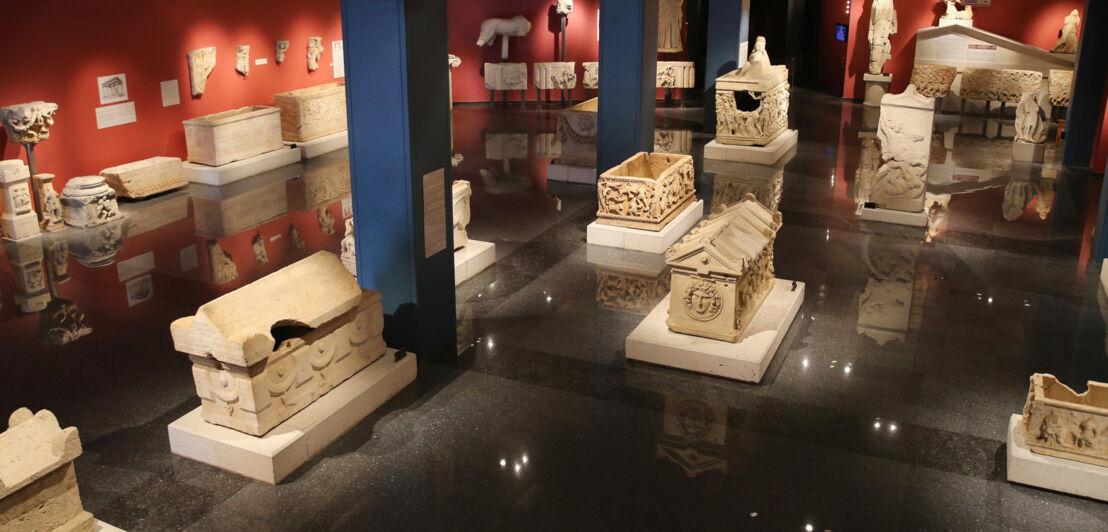 Ein abgedunkelter Ausstellungsraum eines Museums mit zahlreichen Artefakten und Statuen.