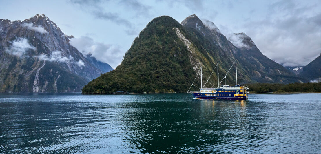 Ein Schiff auf dem Wasser inmitten einer wolkenverhangenen Fjordlandschaft. 