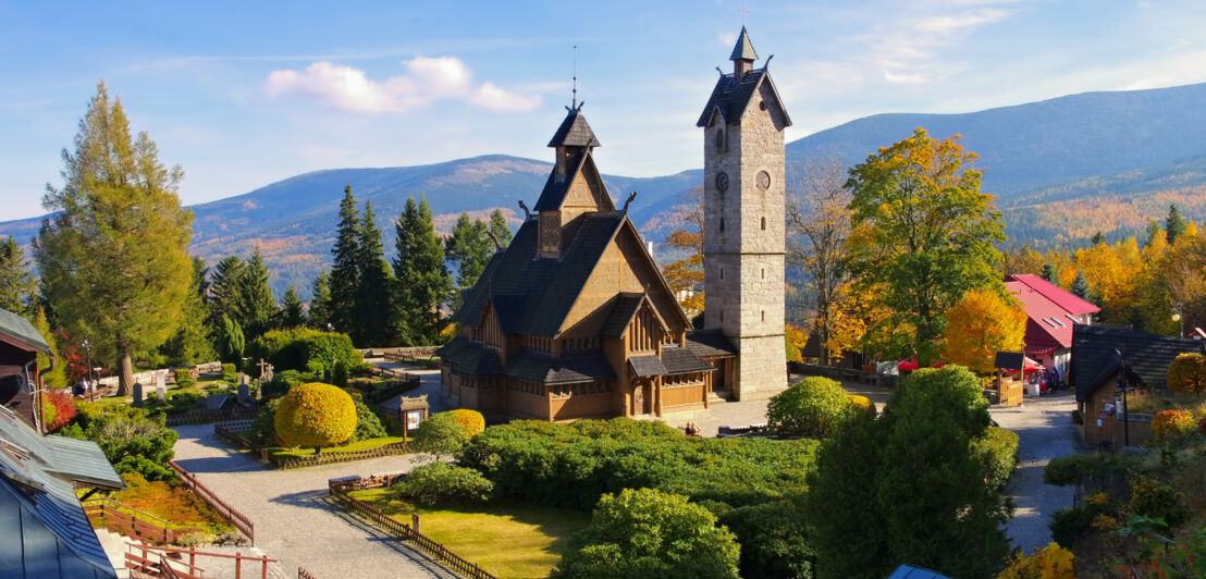 Eine mittelalterliche Stabholzkirche in einer Parkanlage vor Gebirgskette.