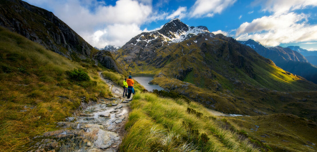 Zwei Personen in Wanderkleidung oberhalb eines Sees in einer Berglandschaft.