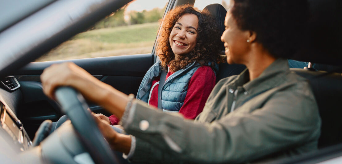 Zwei gut gelaunte Frauen auf den Vordersitzen eines fahrenden Autos.