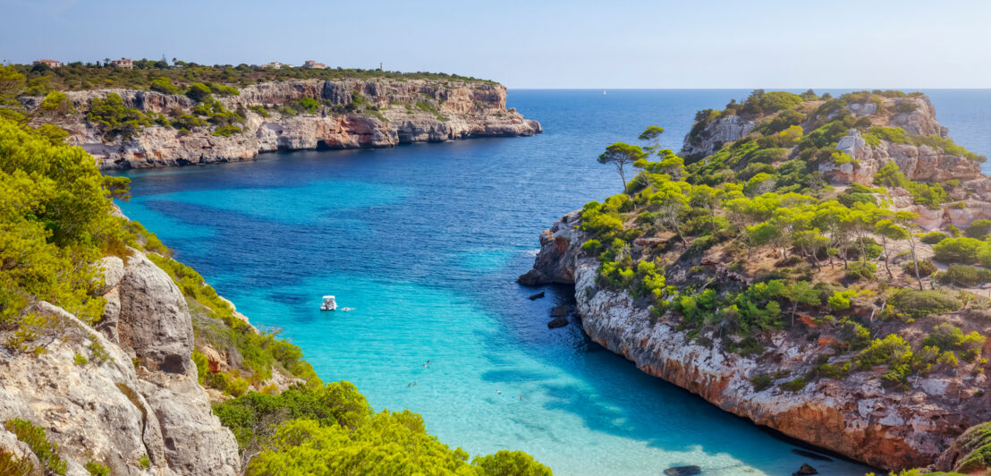 Einsame Badebucht mit Boot im türkisblauen Wasser an einer mediterranen, bewaldeten Felsküste.