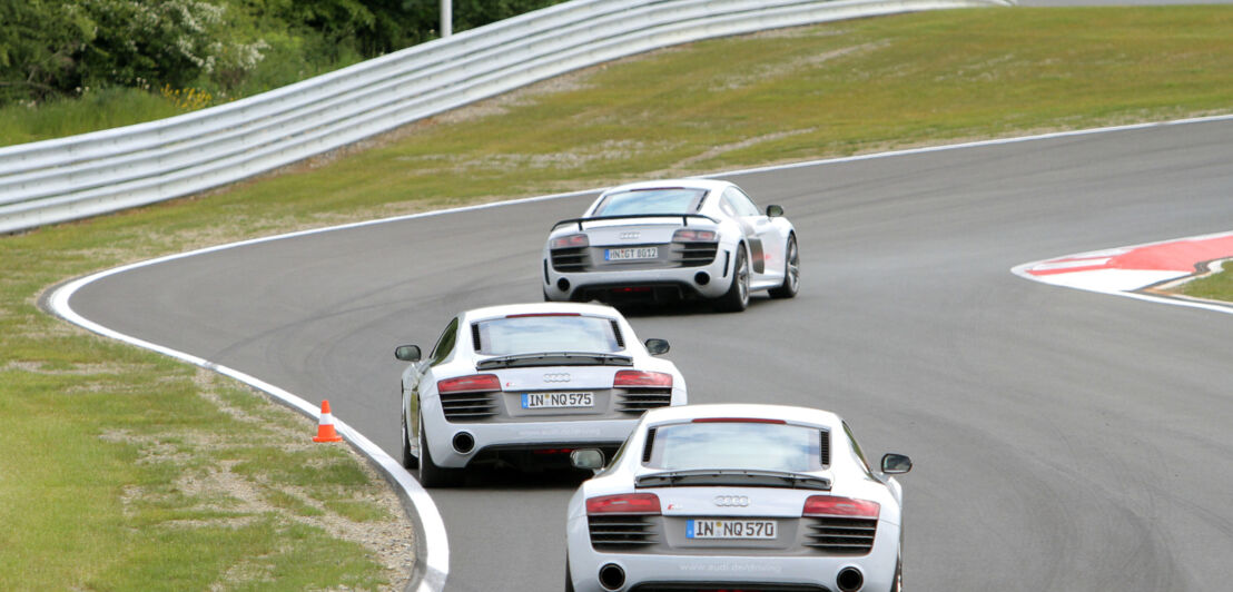 Drei weiße AUDI-Sportwagen fahren hintereinander auf einem kurvigen Parcours.