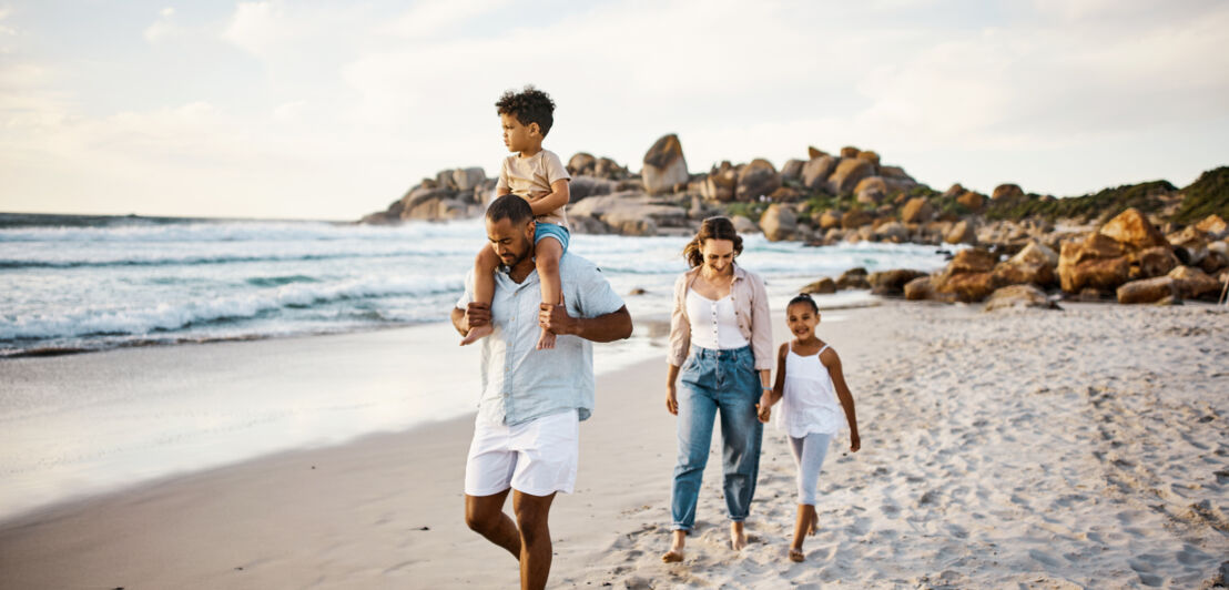 Eine junge Familie mit zwei Kindern spaziert auf einem Sandstrand am Meer entlang