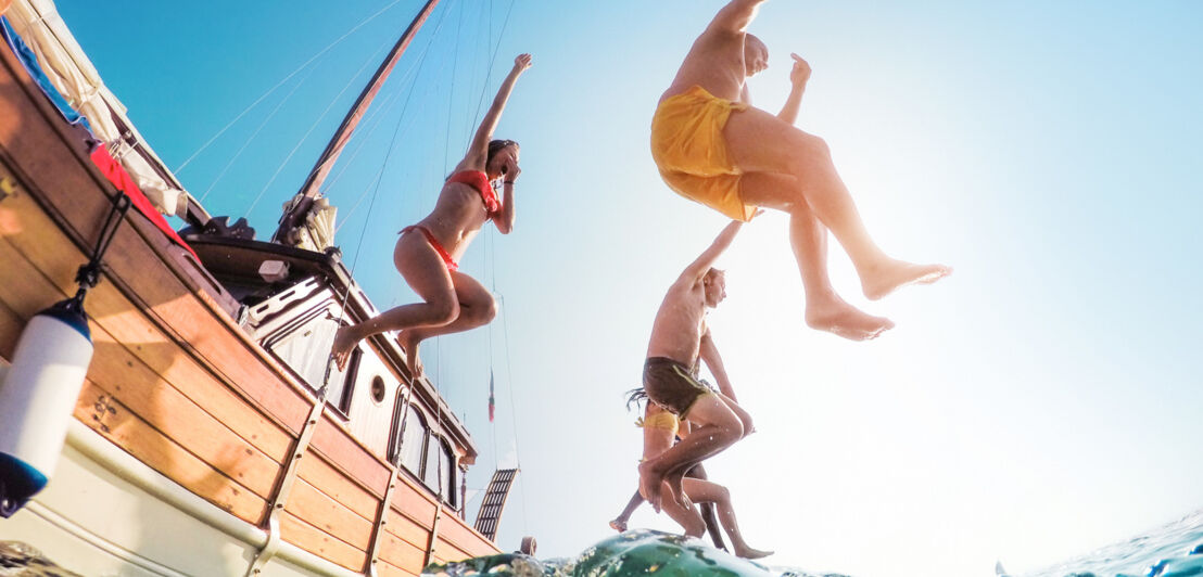 Untersicht einer Personengruppe, die in Badekleidung von einem Segelboot ins Wasser springt