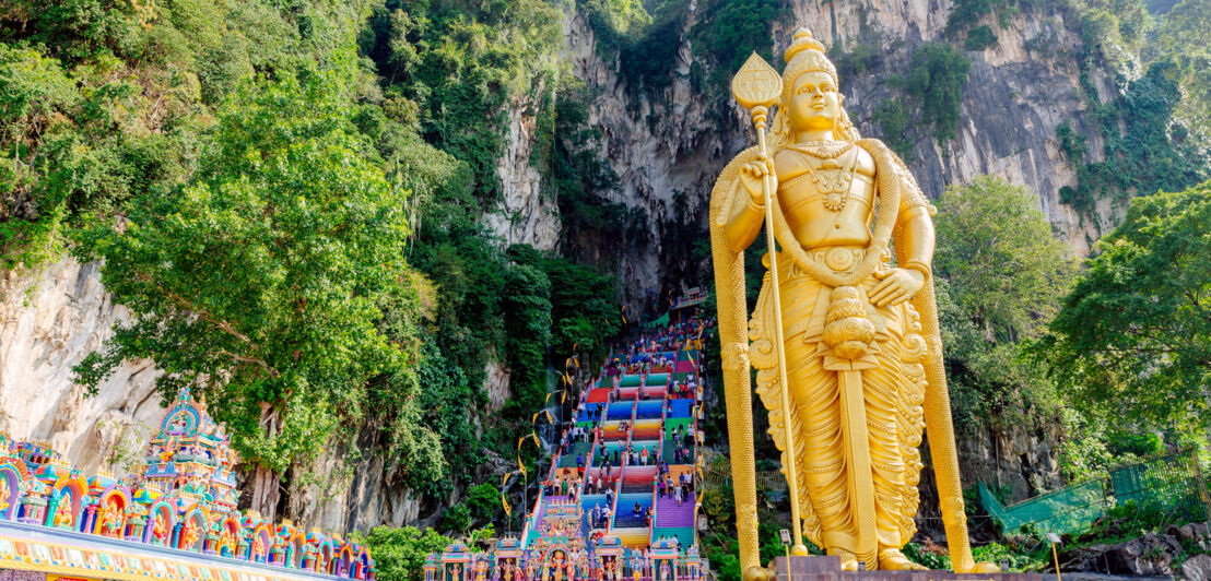 Goldene Statue vor einer großen Treppe mit bunten Stufen, die in eine Felsenhöhle hineinführen.