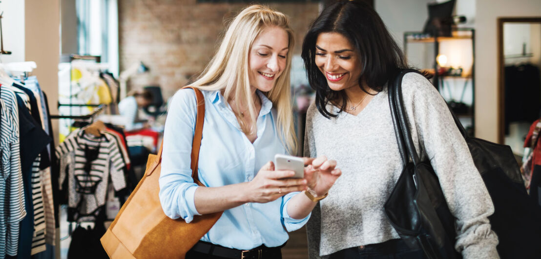 Zwei Frauen schauen gemeinsam auf ein Smartphone in einer Modeboutique.