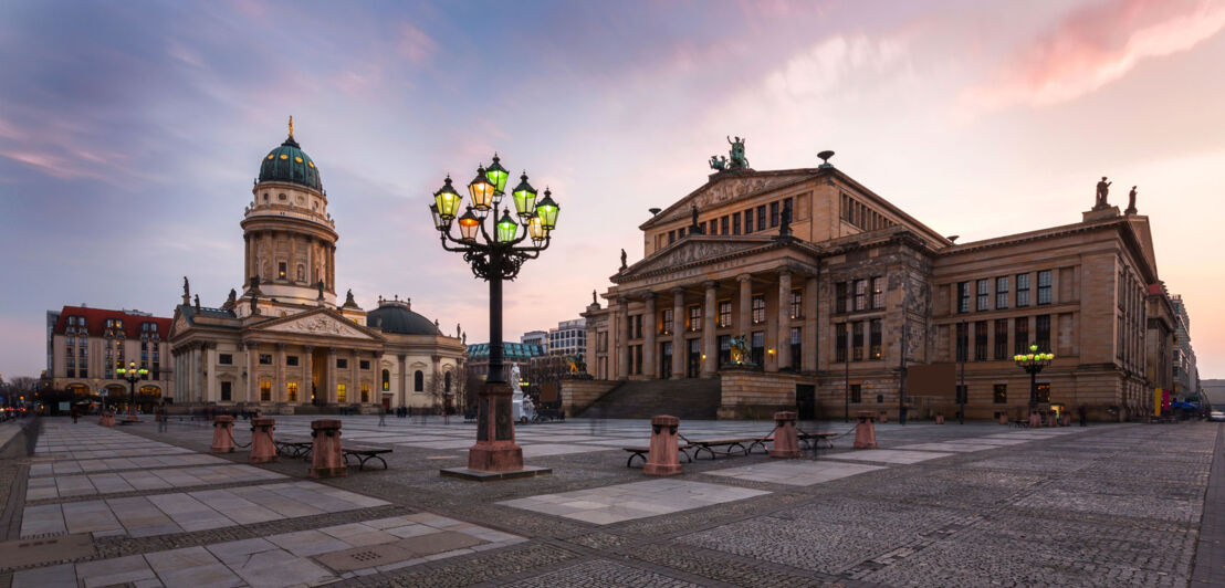 Der Berliner Gendarmenmarkt mit Dom und Schauspielhaus bei Abenddämmerung.