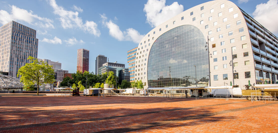 Blick von oben auf eine Stadt mit einer grünen Wiese, Hochhäusern und einer modernen, hufeisenförmigen Markthalle.