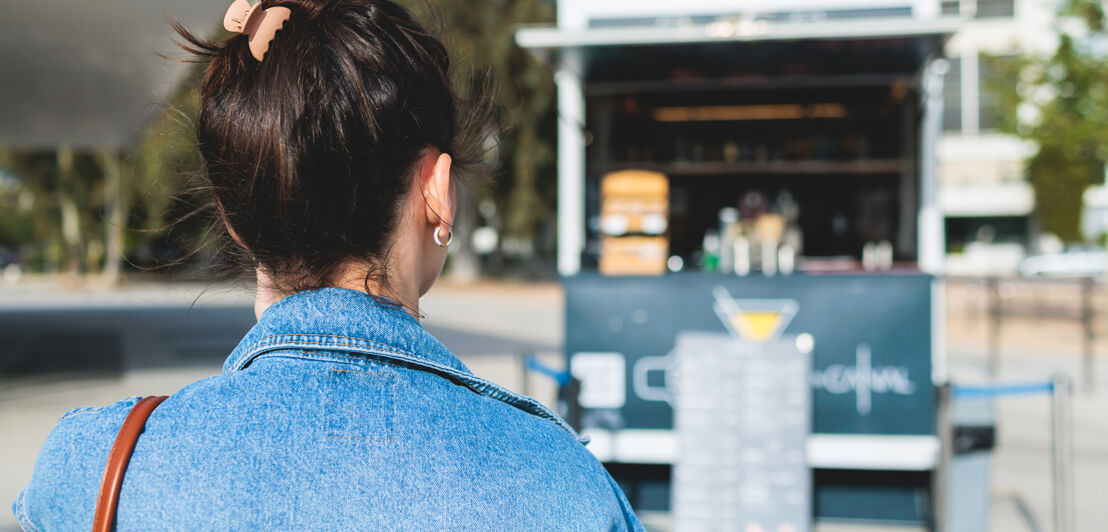 Girl choosing and ordering street food in colourful food truck van on a festival in a city park, summer sunny day, food stall kiosk offers fast food lunch, coffee and drinks for sale