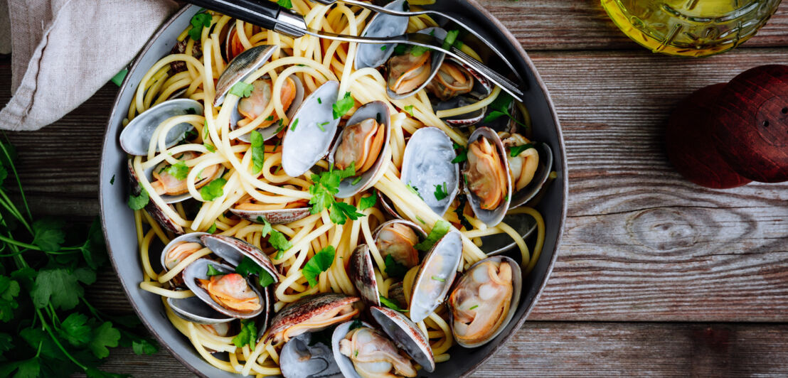 Aufsicht einer Schale mit Spaghetti und Venusmuscheln auf einem Holztisch.