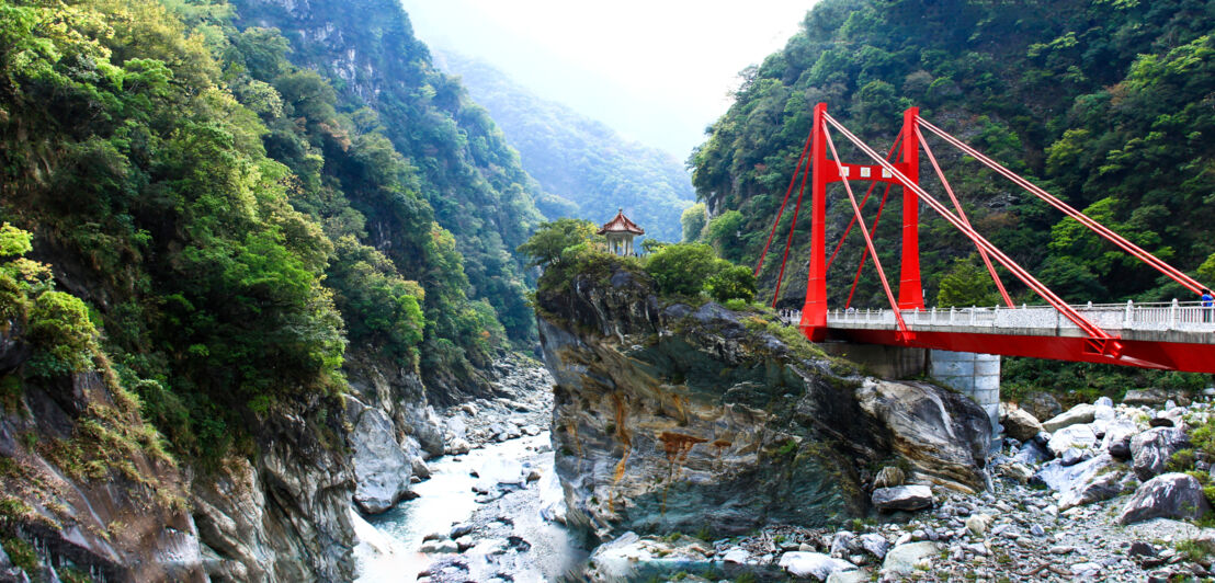 Eine Schlucht an einem Fluss mit roter Hängebrücke.