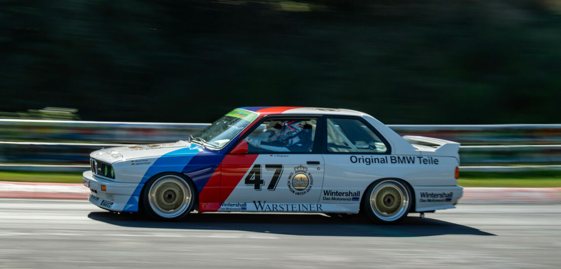 Ein fahrender BMW M3 E30 Rennwagen auf einer Straße.