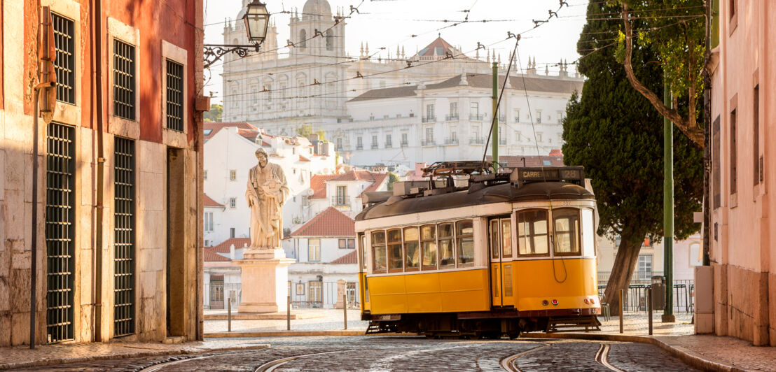 Straße mit Schienen in Lissabon, auf denen eine gelbe Tram fährt.