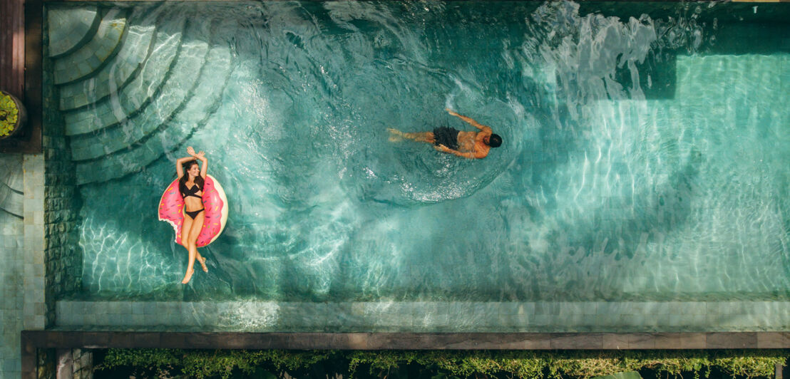 Ein Paar in einem luxuriösen Swimmingpool aus der Vogelperspektive.