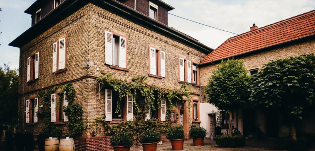 Renoviertes Gutshaus aus Backstein mit weißen Fensterläden und grünen Pflanzen.