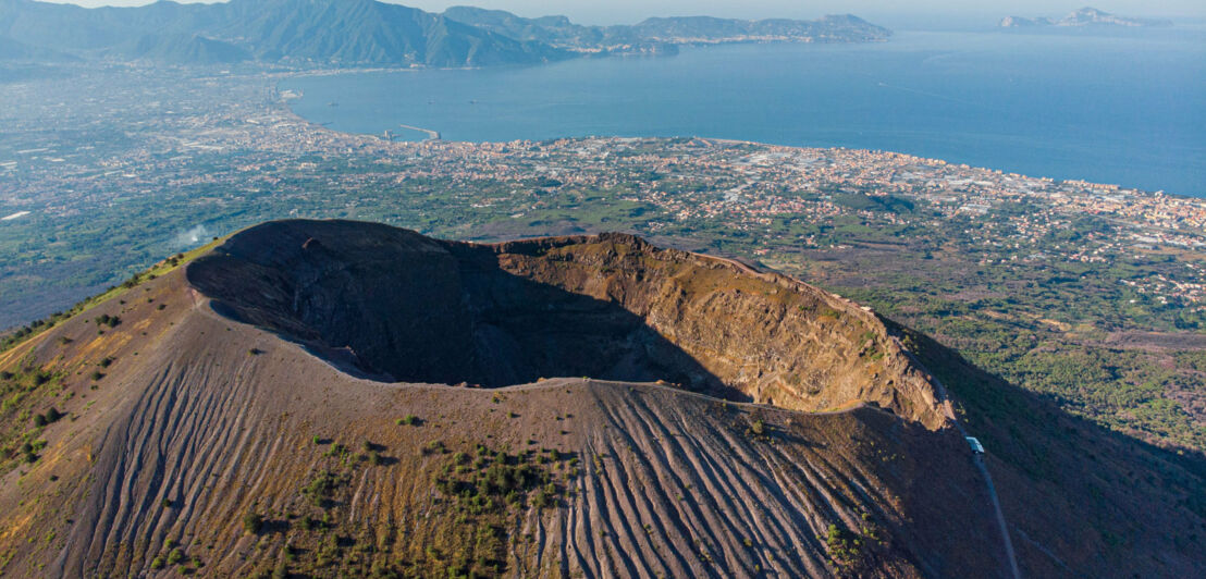 Luftaufnahme des Kraterrandes des Vesuvs mit Neapel und Meer im Hintergrund.