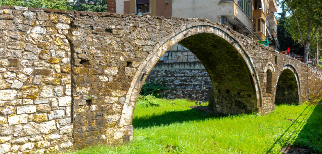 Steinbogenbrücke über einem ehemaligen Flusslauf Grasfläche in einem Stadtgebiet.