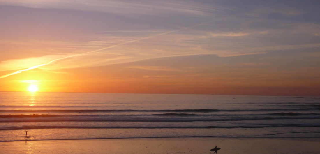 Sandstrand am Meer mit leichten Wellen bei Sonnenuntergang.