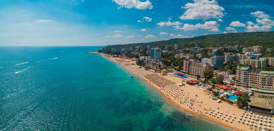 Stadt am Meer mit breitem Sandstrand mit Sonnenliegen in Reih und Glied.