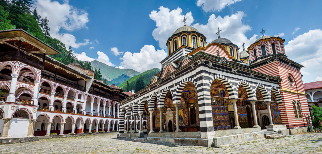 Farbenfrohe orthodoxe Klosteranlage mit mehreren Gebäuden im Gebirge.