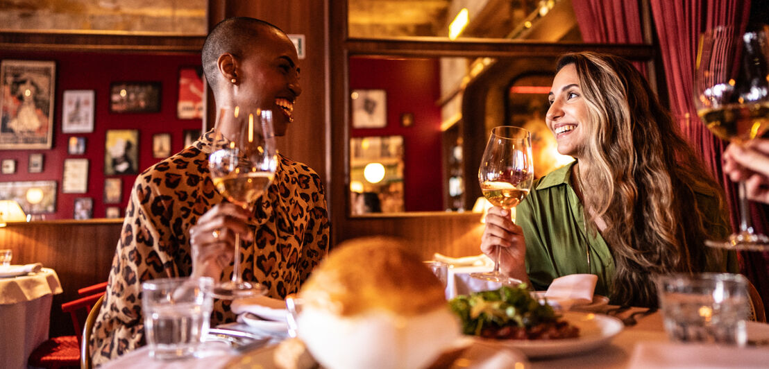 Zwei gut gelaunte Frauen an einem Tisch beim Dinner in einem Restaurant.