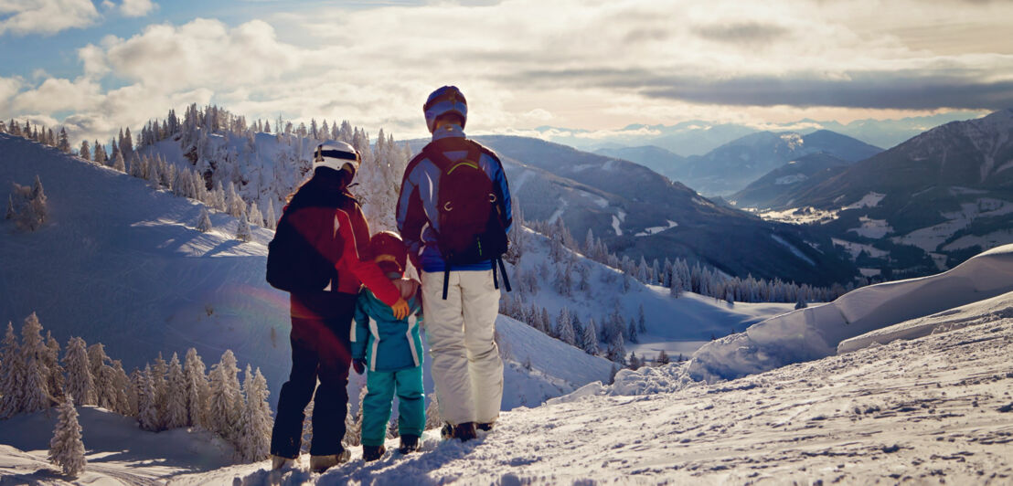 Drei Personen, darunter ein Kind, stehen auf einer Skipiste.