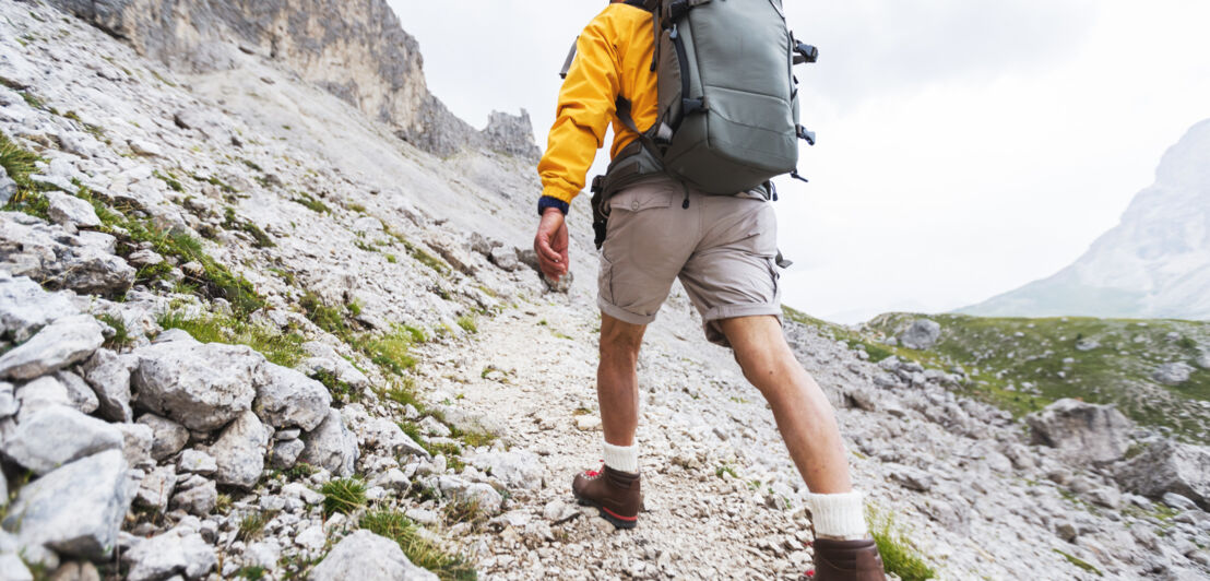 Wandernde Person von hinten in einer kargen Berglandschaft. 