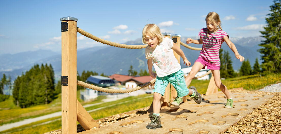 Zwei Kinder laufen auf einem Parkour in einer Berglandschaft.