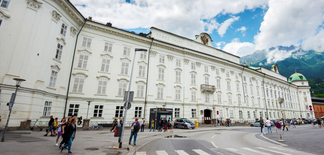 Imposantes weißes Gebäude im spätgotischen Stil in einer Stadt vor Bergpanorama.